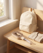 Brumelle Hydrating Brush in beige on a wooden bench beside a cream backpack and folded towel