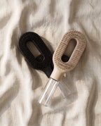 The Brumelle Hydrating Brush in black and in beige crossed on linen, photographed from above with both clear refillable mist reservoirs visible