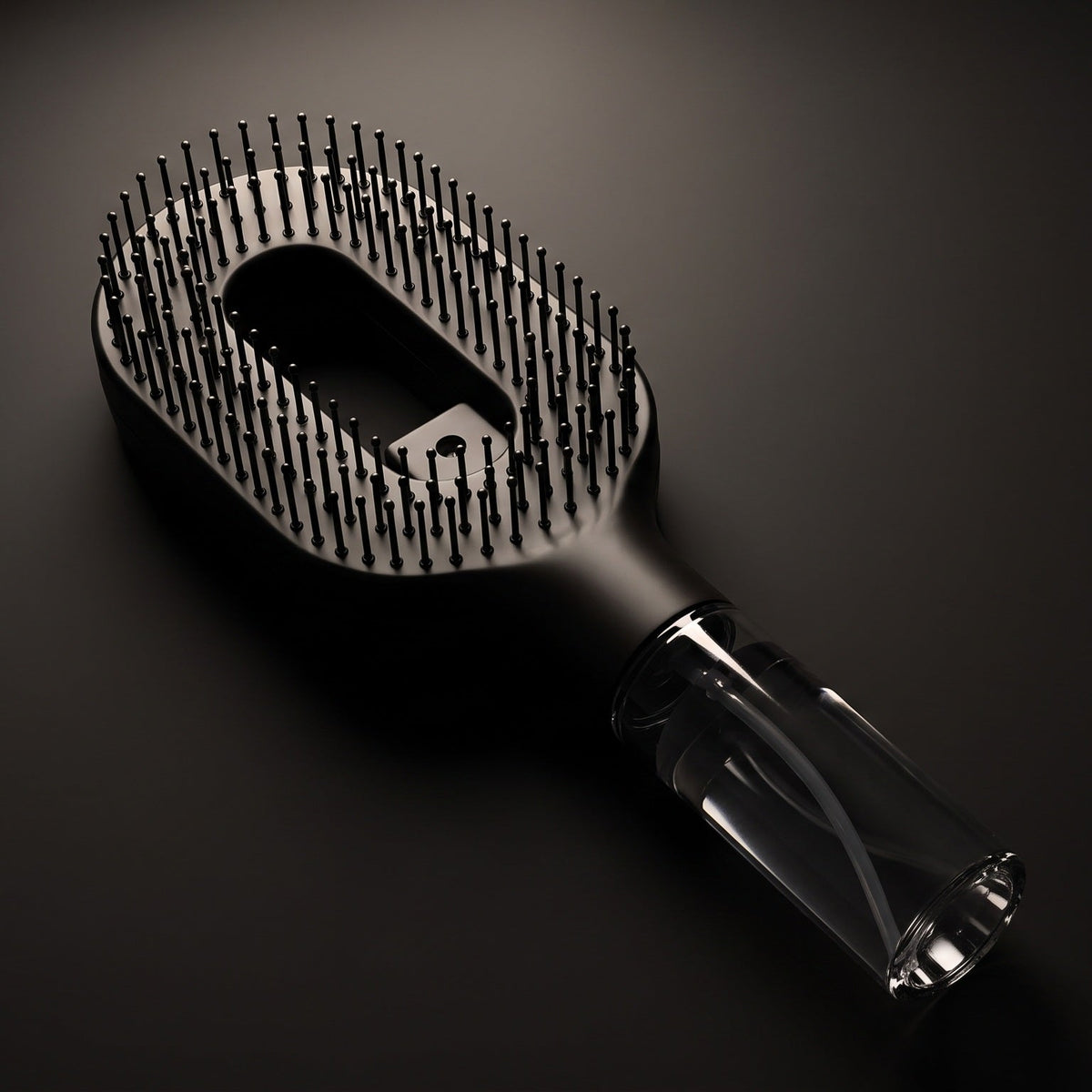 Brumelle Hydrating Brush in black, lit from above to show the clear refillable mist reservoir in the handle
